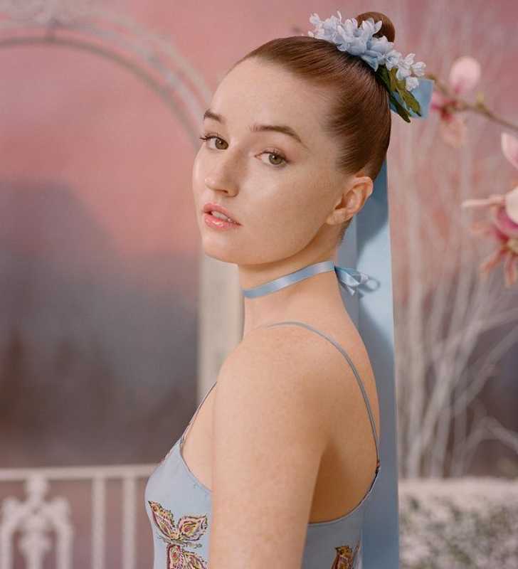 Picture of Kaitlyn Dever posing for a photo in a fancy  dress with beautiful background in pink color